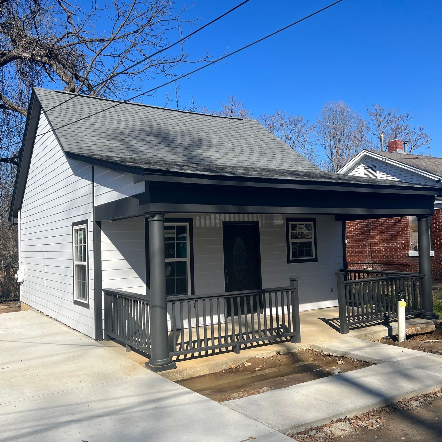 Small gray house with a front porch, black railing, and driveway under a clear blue sky