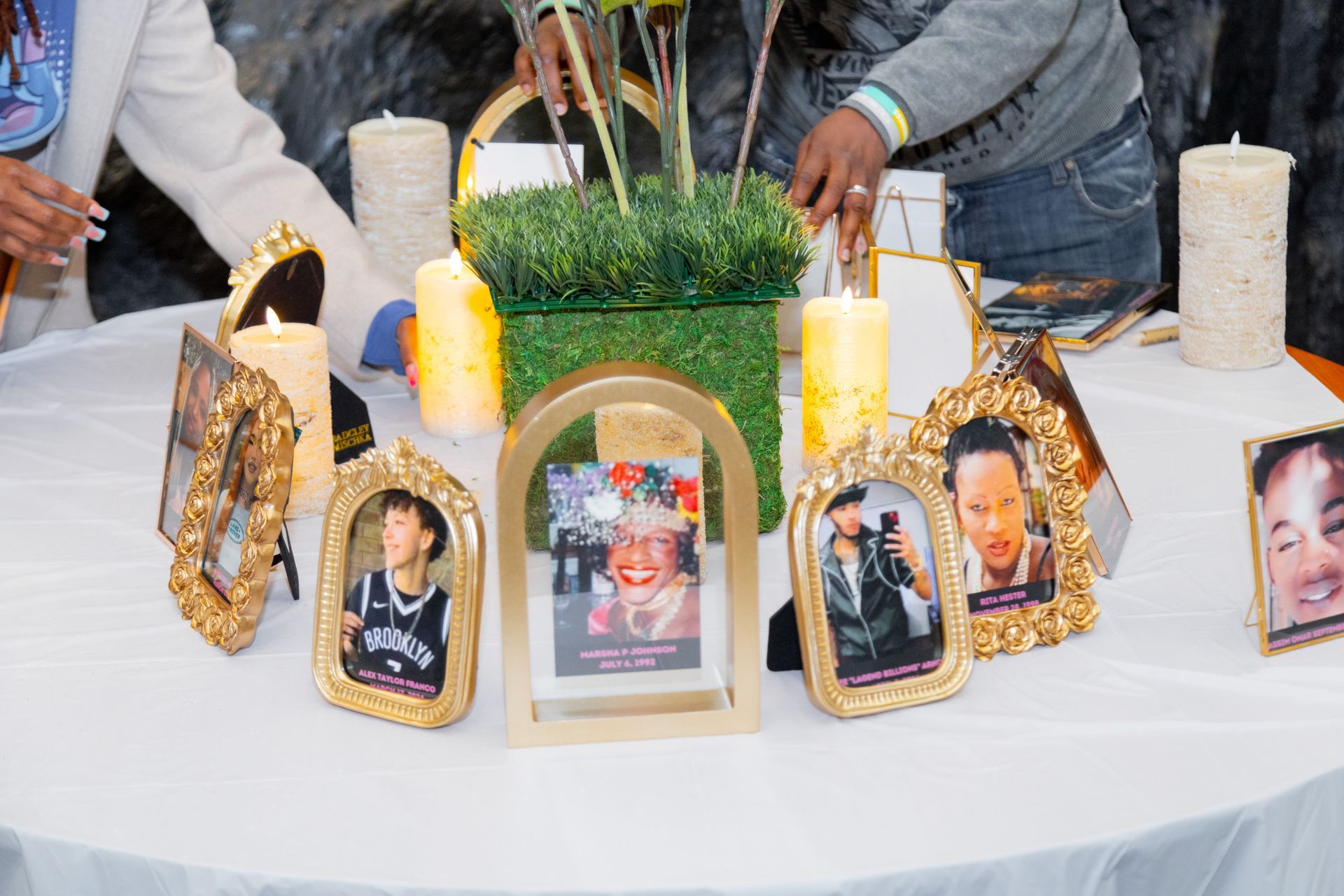 Memorial table with framed photos, candles, and greenery on a white cloth