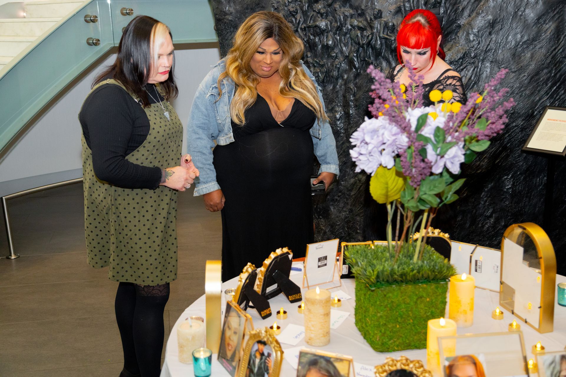 Three women stand by a decorated table with flowers, gold mirrors, and perfume bottles in a store-like setting