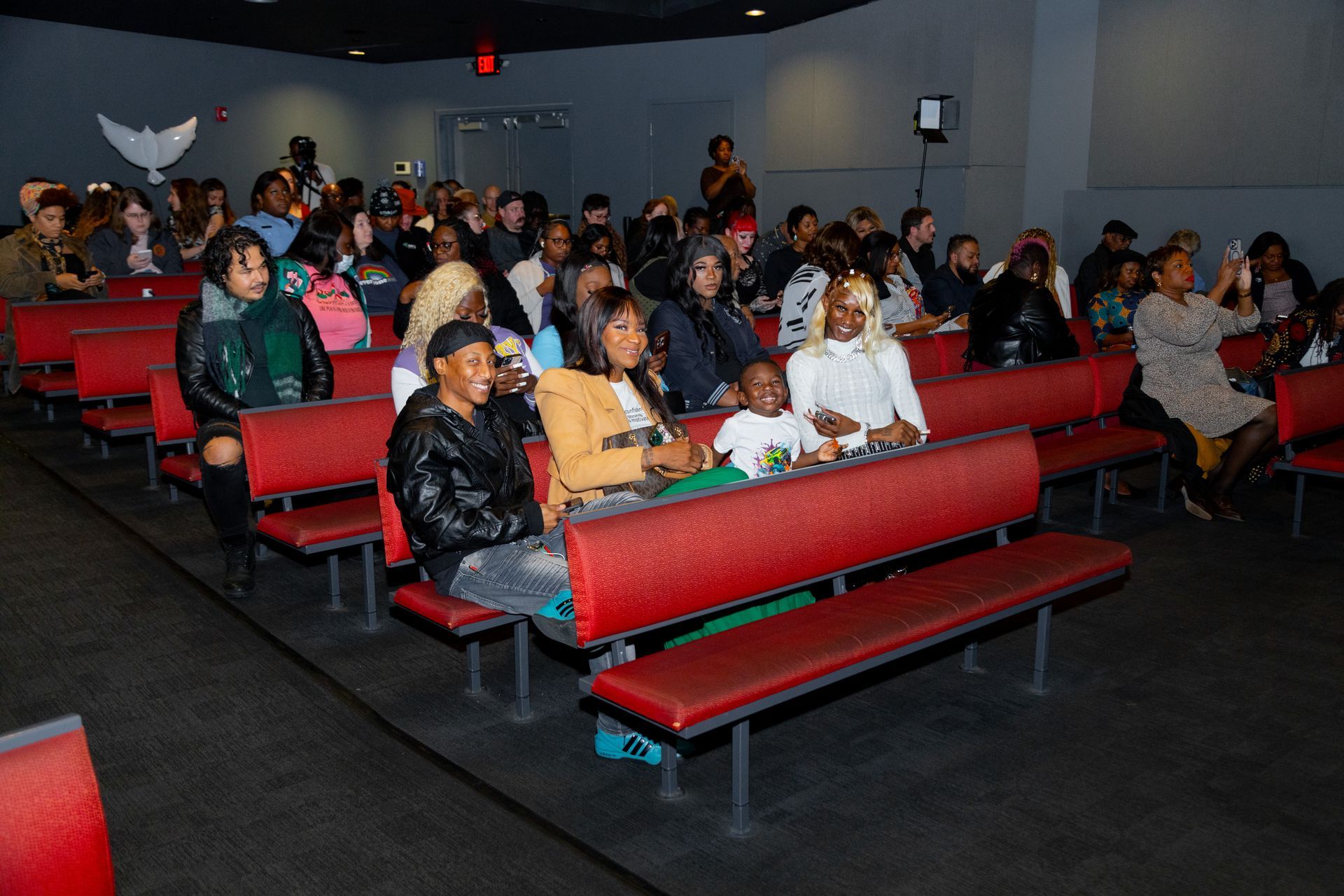 People seated on red benches in a dimly lit movie theater, facing the screen
