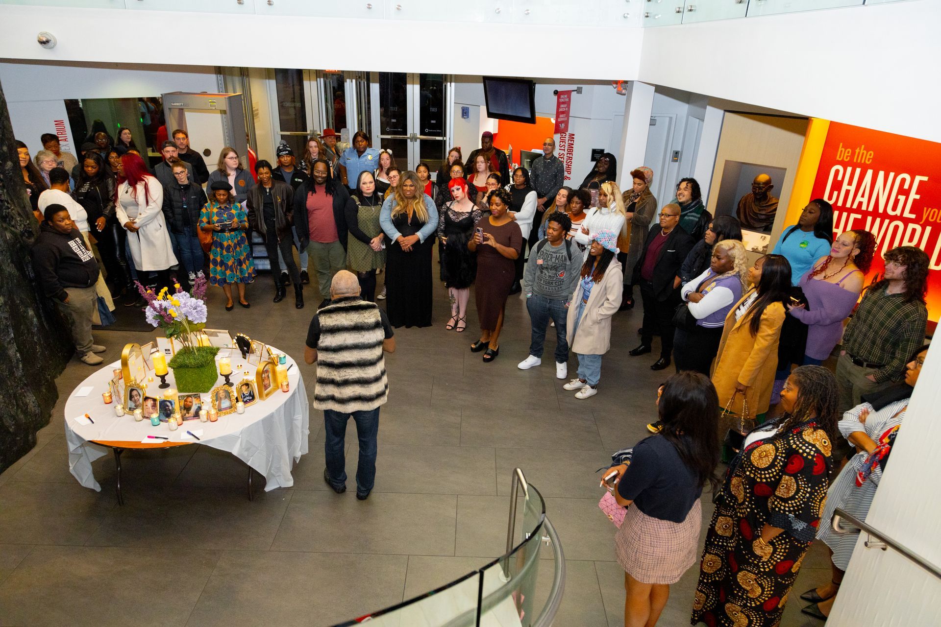 Crowd gathered in a bright lobby around a display table and orange “CHANGE” banner at an event reception