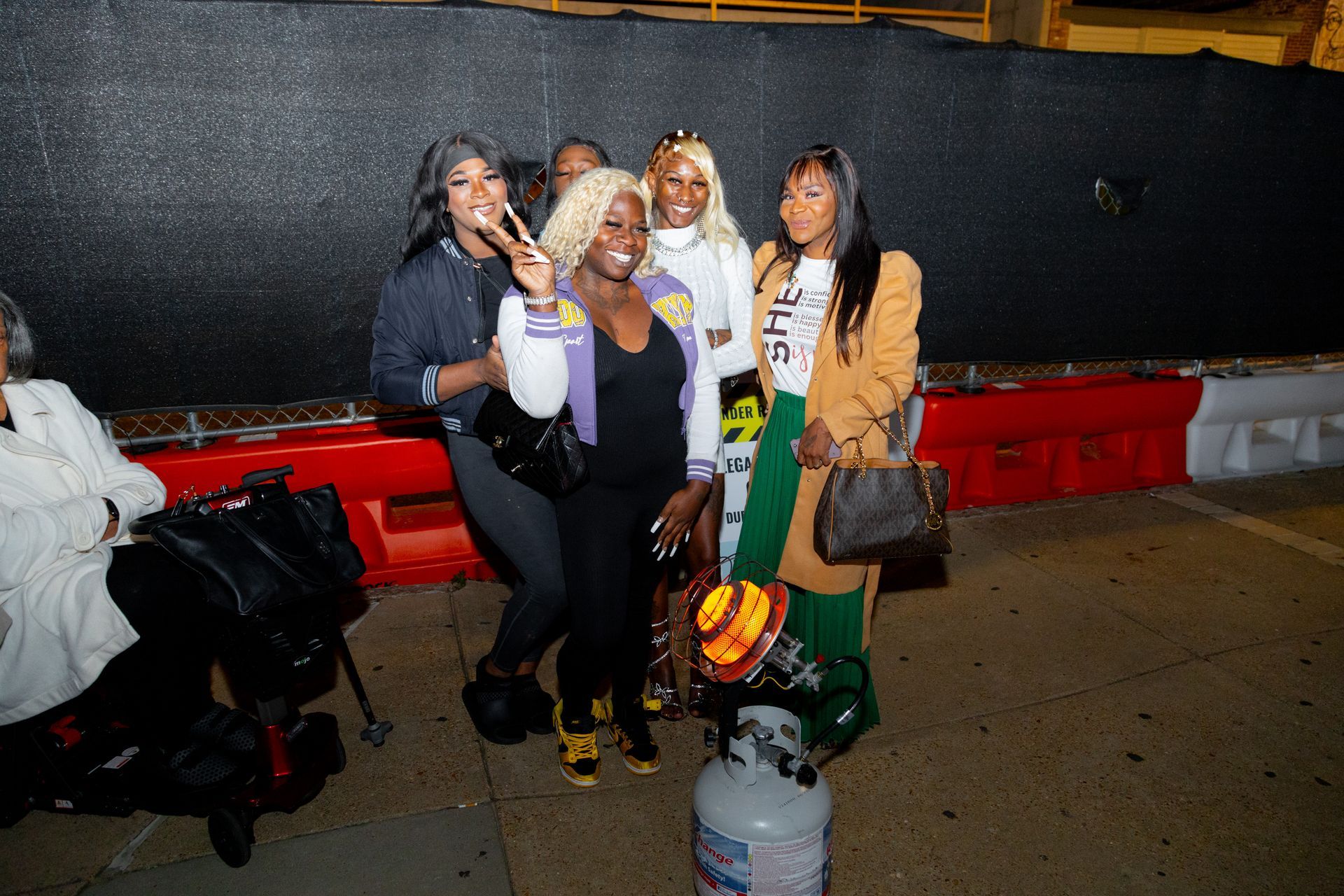 Four people posing beside a red bench at night, smiling and holding drinks outdoors