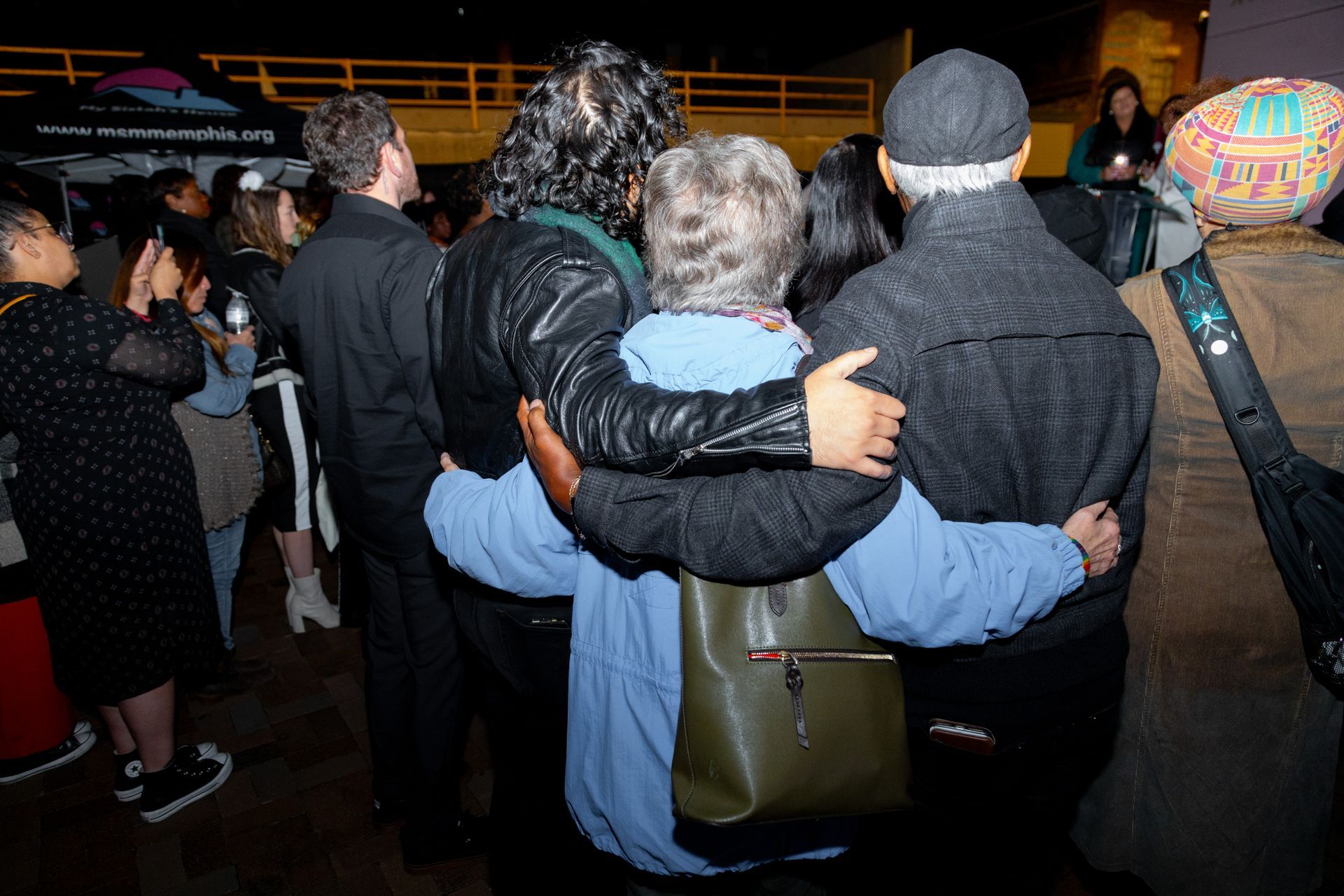 People huddled together at a nighttime outdoor event, seen from behind.