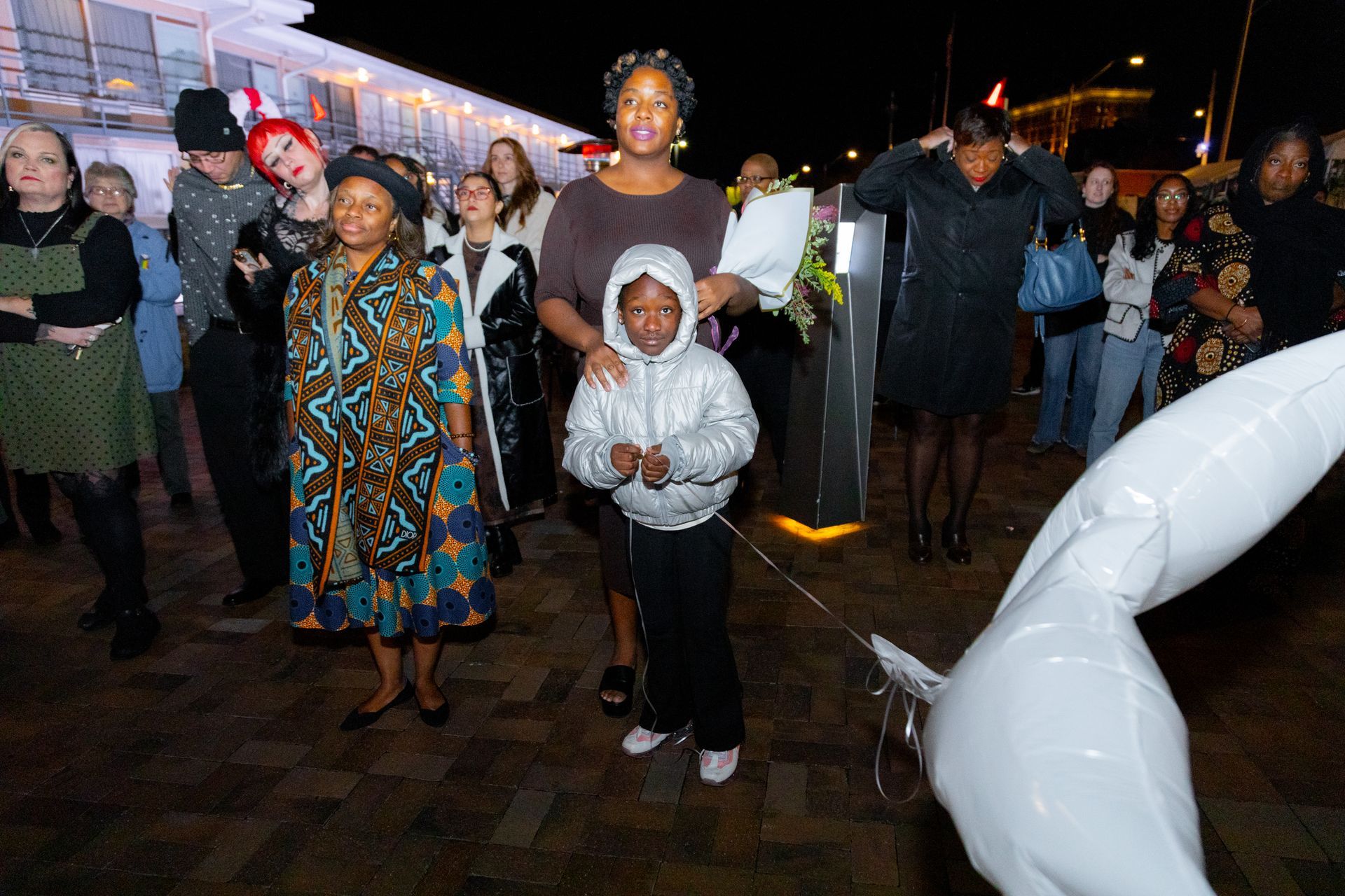 People standing at a nighttime outdoor event, with one child in a gray hoodie in front.