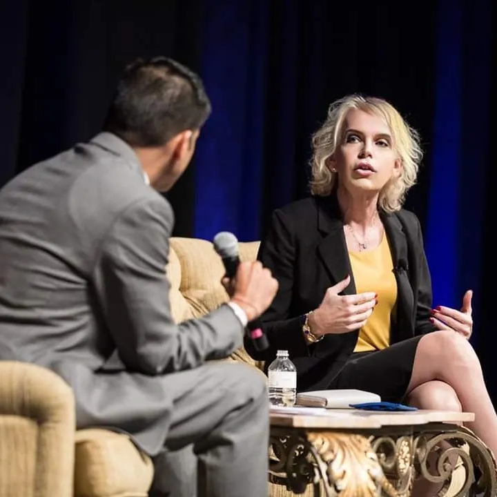 Two speakers in conversation on stage, seated with microphones, against a dark blue backdrop.