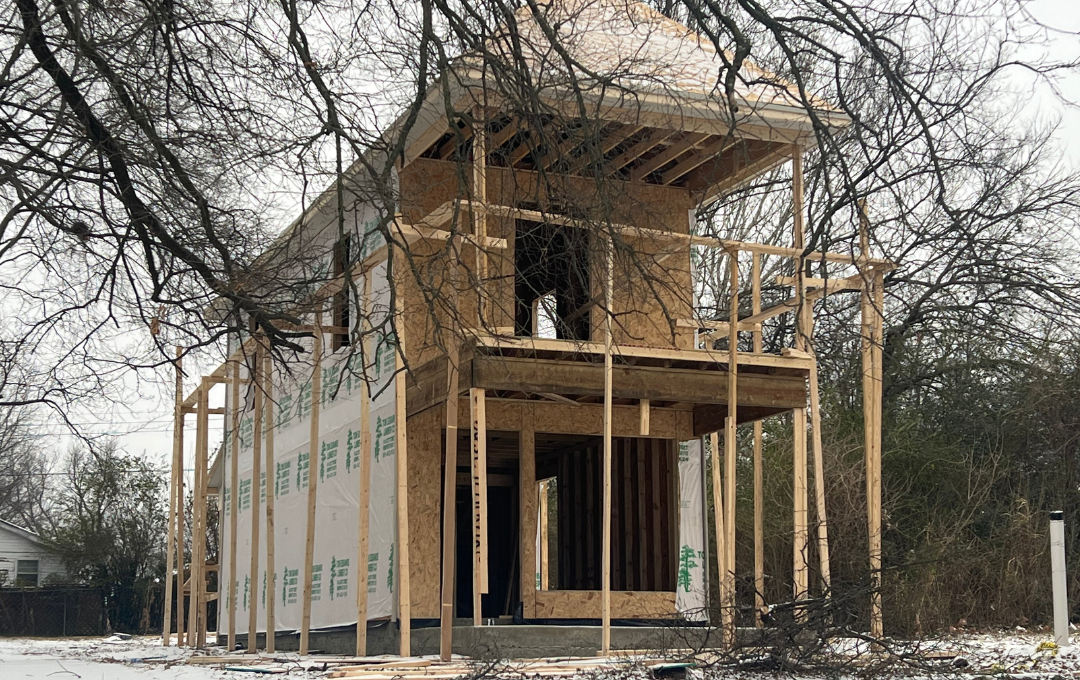 Two-story house under construction with exposed framing and snow on the ground