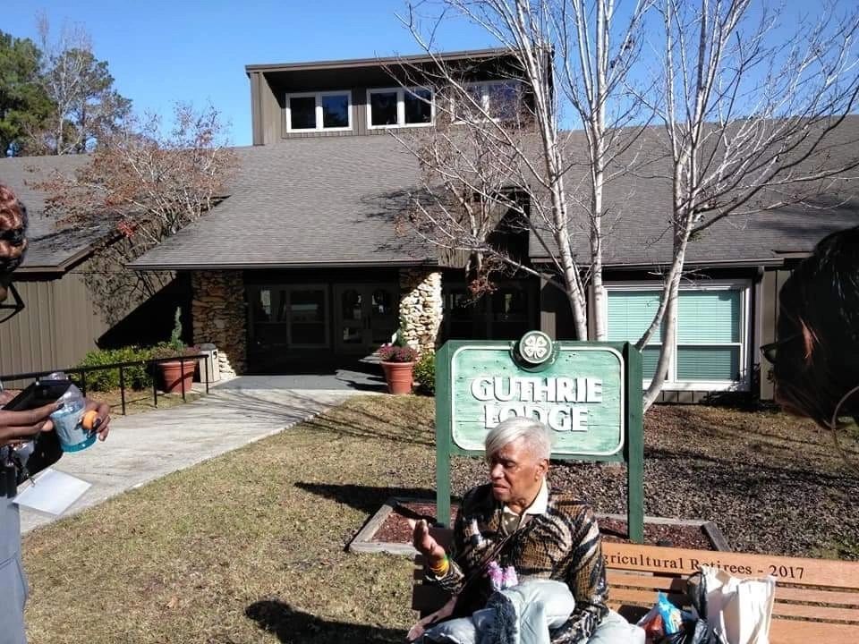 Person sitting outside a Guthrie sign in front of a house, holding a drink