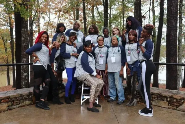 Group of people posing outdoors in a wooded area, wearing matching gray and navy outfits.
