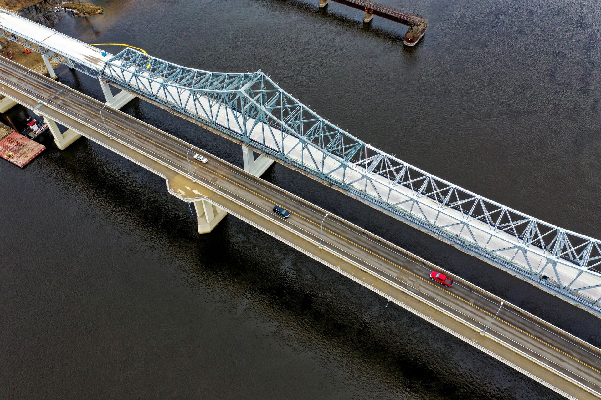 Aerial view of two bridges crossing a dark river, with a red car on the lower bridge.