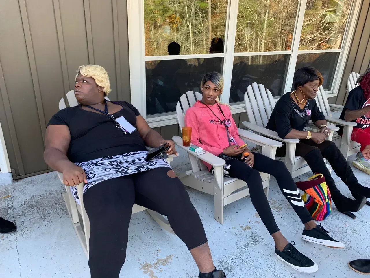 Three people sitting in chairs on a porch, one wearing a pink shirt and another holding a bag.