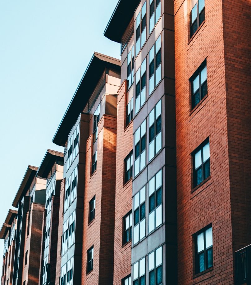 Multi-story brick apartment building with many windows against a light blue sky.