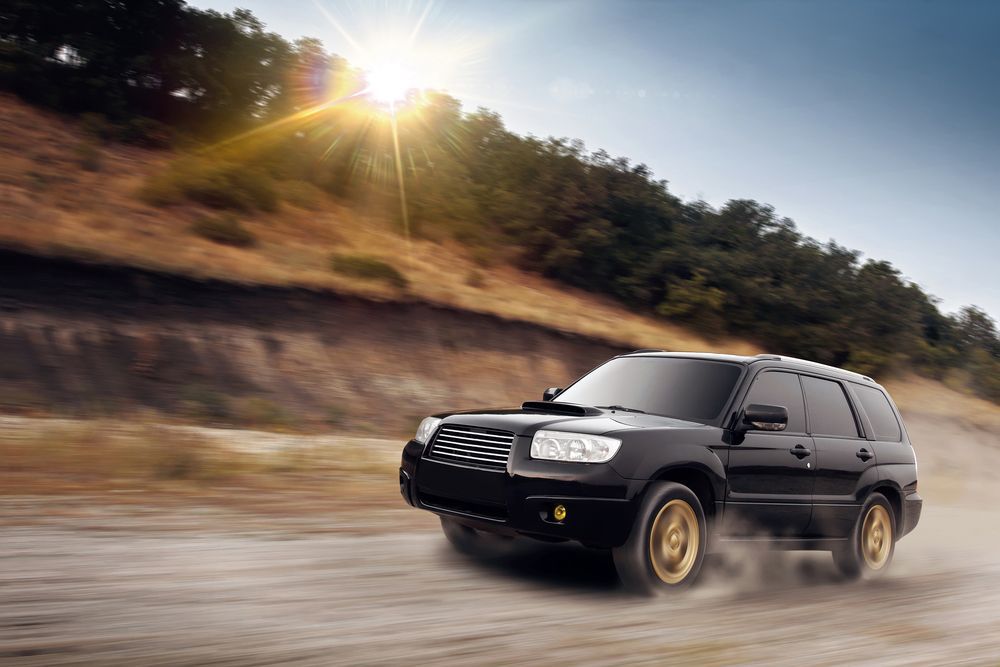 A black suv is driving down a dirt road.