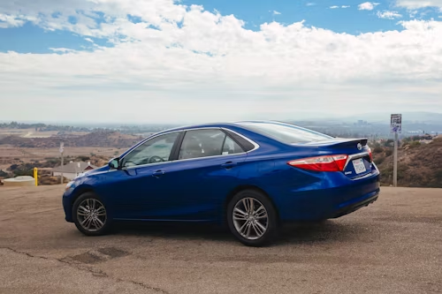 Blue sedan parked on a scenic overlook with a city and mountains in the background