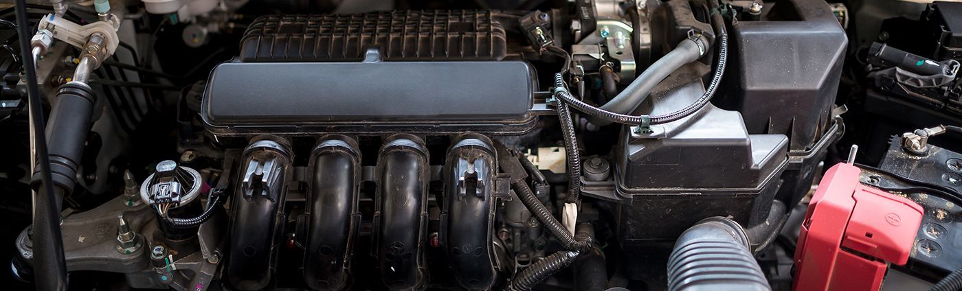 An overhead view of an internal combustion engine inside a vehicle's engine bay, showing intake runners and components.