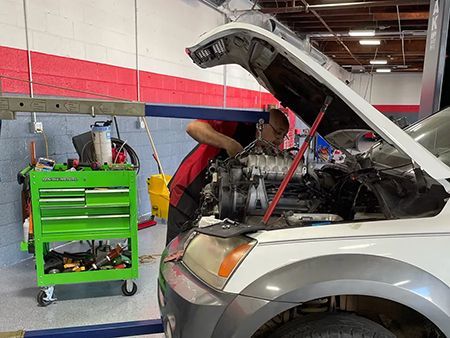 Mechanic working on a white car engine in a garage.