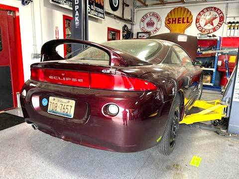 A red eclipse is sitting on a lift in a garage.