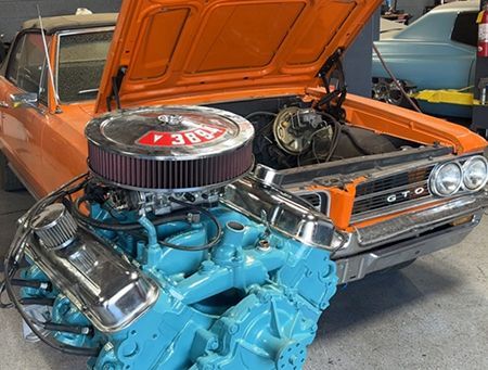 Classic orange Dodge muscle car with hood open, showing a bright blue engine and chrome air cleaner.