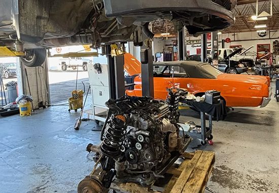 Car workshop with a lifted vehicle and a detached engine on a stand, orange classic car in the background