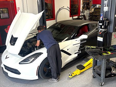 Mechanic working on a white and black sports car with the hood open in a garage.