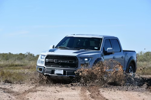 Silver Ford Raptor truck driving through muddy terrain.