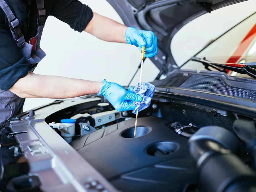 Mechanic in blue gloves checking car oil with dipstick in engine bay.