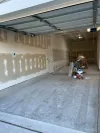 A garage interior with taped and mudded drywall, construction equipment, and tools on the floor.