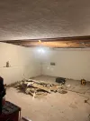 A room undergoing renovations with exposed ceiling joists and construction debris on the floor.