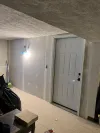 A white six-panel door installed in a basement with unfinished drywall, a textured ceiling, and a speckled floor.