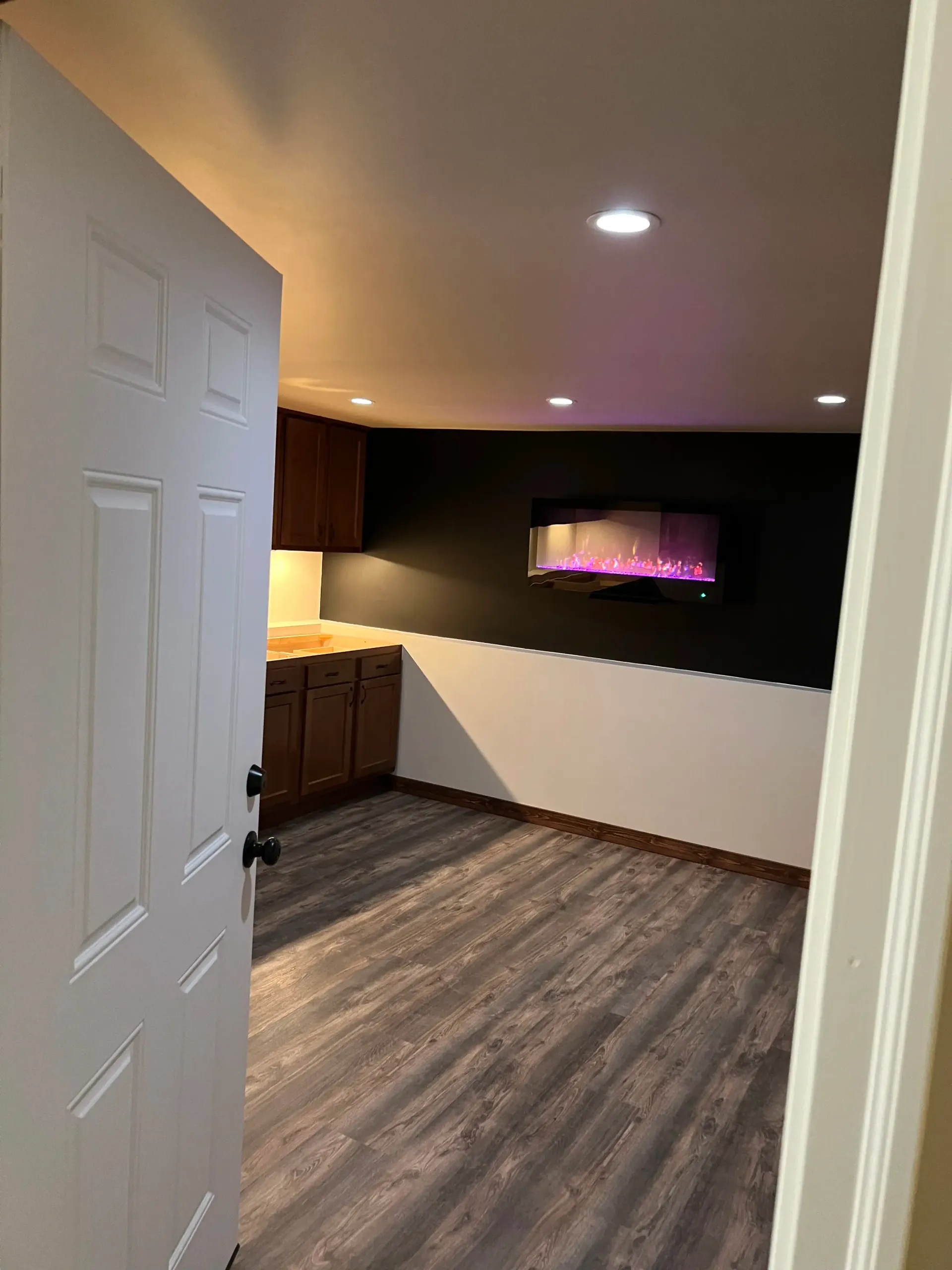 Two chairs and a small table arranged beneath a wall-mounted fireplace on a dark accent wall in a room with wood flooring.