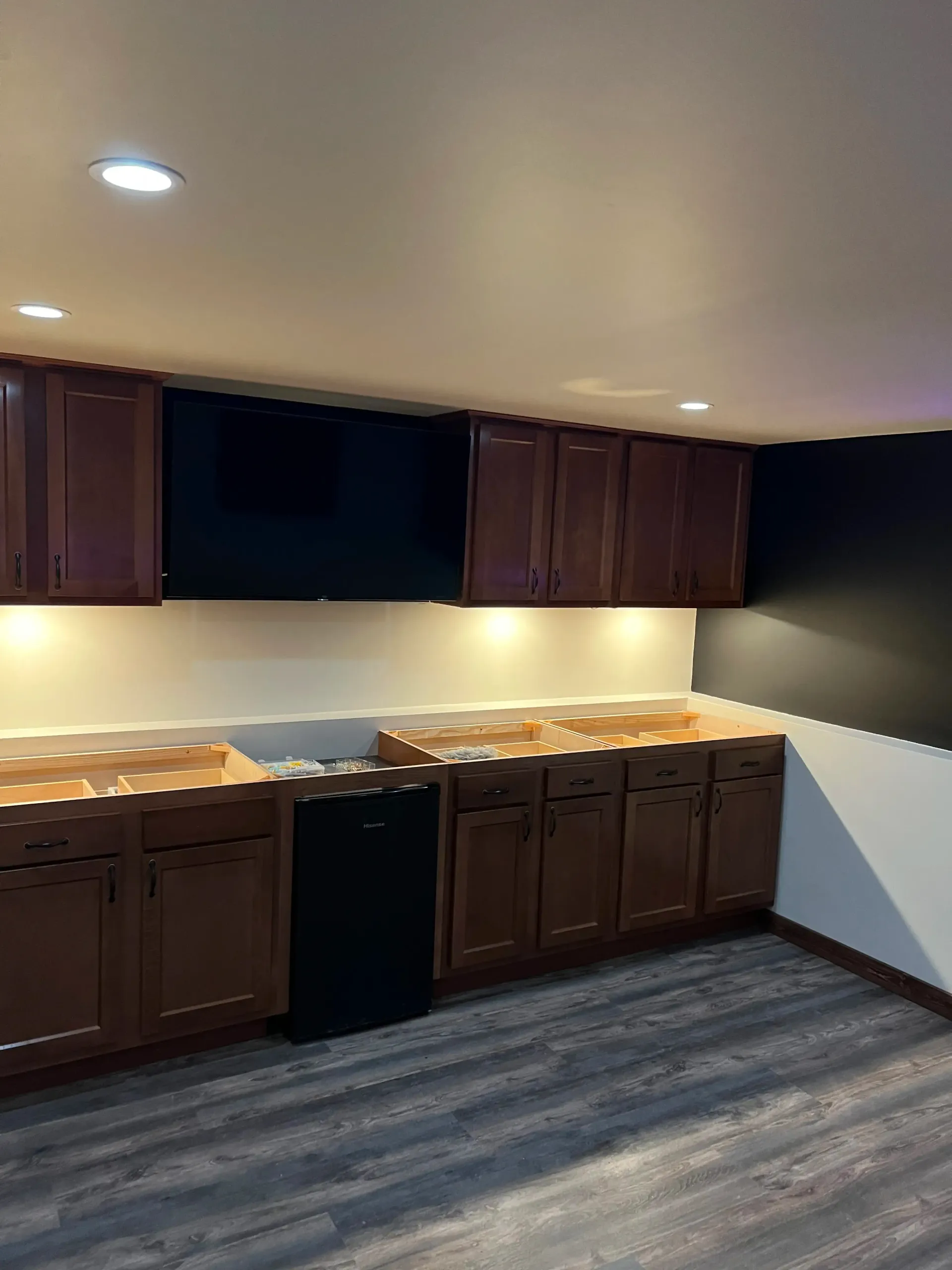 Two chairs and a small table arranged beneath a wall-mounted fireplace on a dark accent wall in a room with wood flooring.