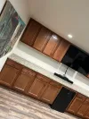 A wooden home bar with granite countertops, upper cabinets, a wall-mounted TV, and a black under-counter refrigerator.