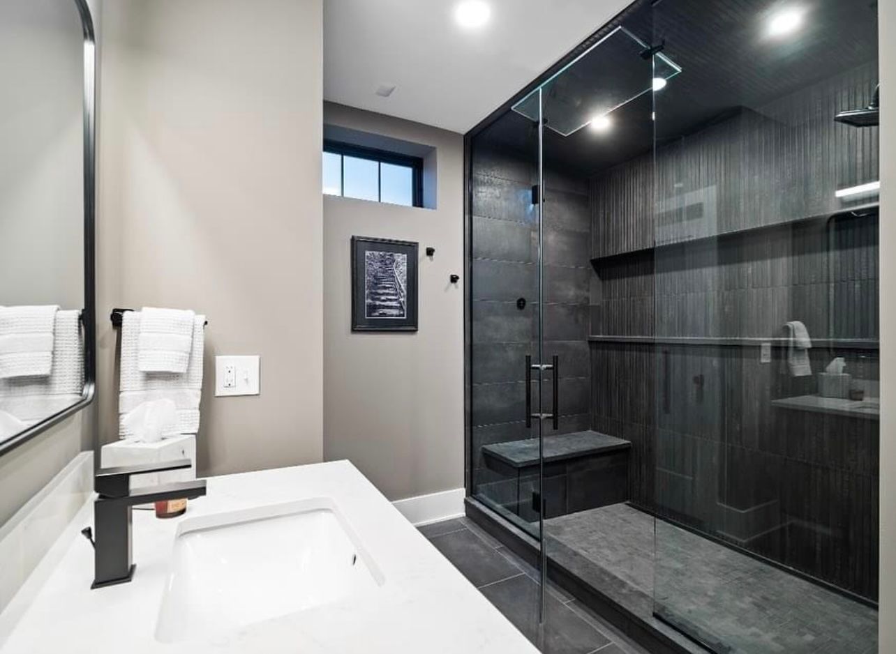 A white hallway with two framed pictures on the wall leads through an open door into a room with dark wood flooring.