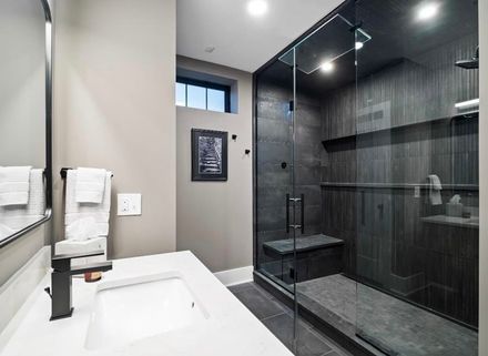 A tiled shower stall with white subway walls, a recessed two-tier shelf, a chrome showerhead, and a stone pebble floor.