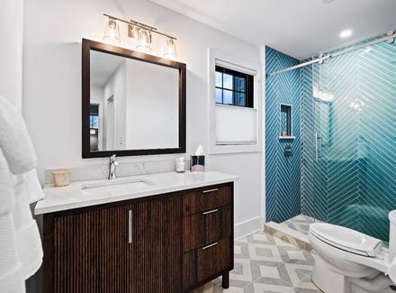 A white freestanding bathtub set on a tiled platform in a corner with two windows above and light-colored tile walls.