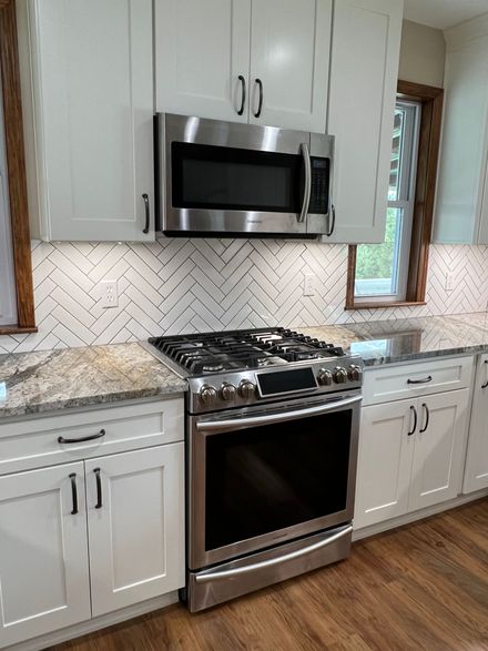 A kitchenette with wood cabinets, granite countertops, a black mini fridge, a mounted TV, and a wicker chair.