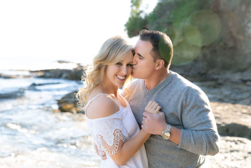 A man is kissing a woman on the cheek on the beach.