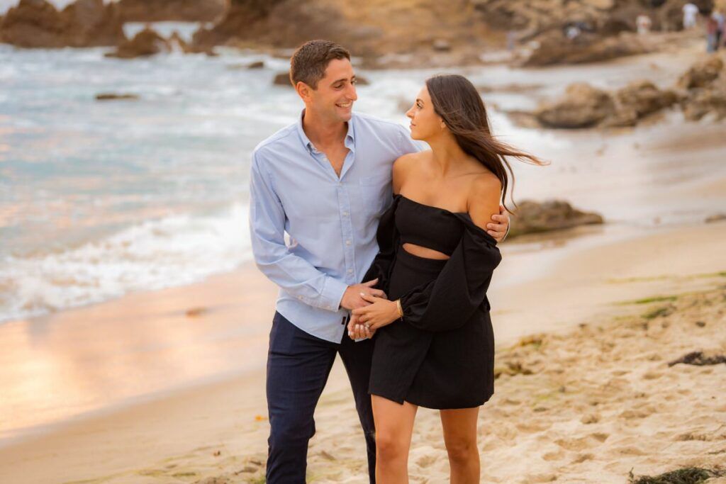 A man and a woman are walking on the beach holding hands on little corona beach in Orange County .