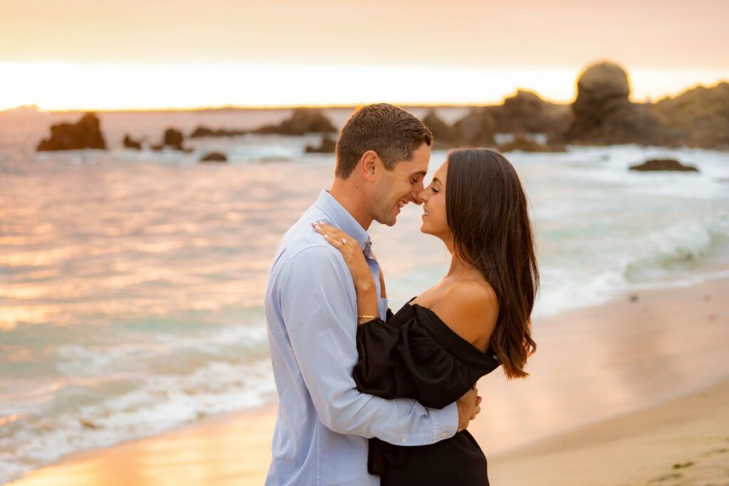 A man and a woman are kissing on the little corona beach at sunset.