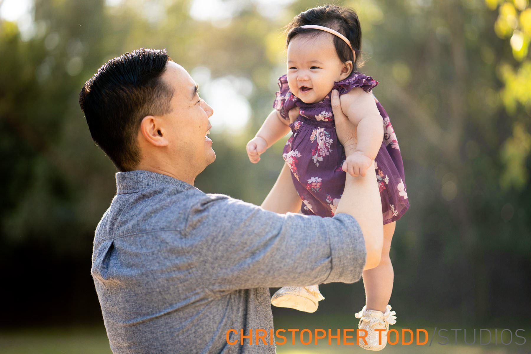 A man is holding a baby in his arms during the fall mini session at Orange County park. 
