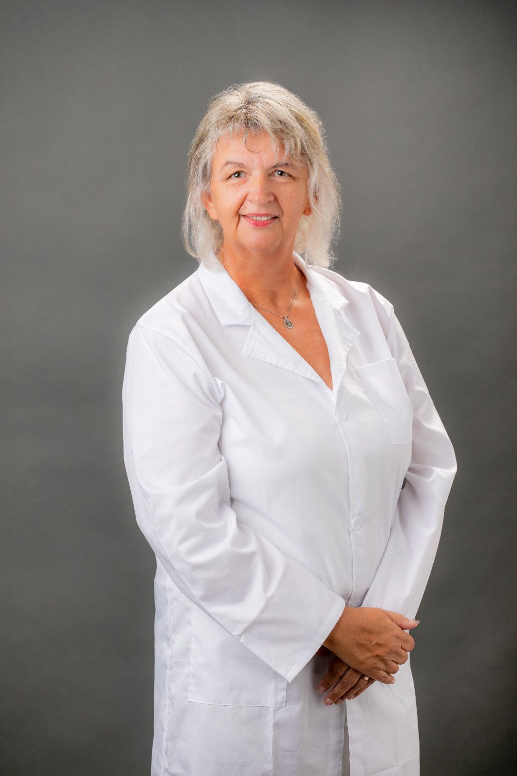 Woman in a white lab coat standing against a gray backdrop, smiling with hands clasped Irvine, Ca 