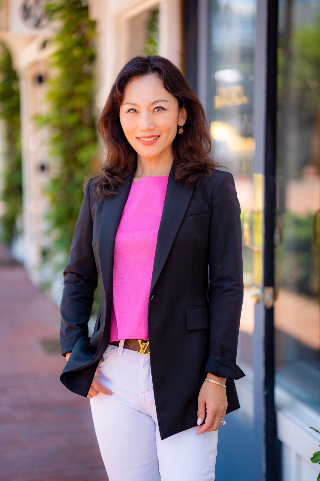 Woman in a black blazer and pink top standing outdoors by a building, smiling at the camera, Lido Island realtor