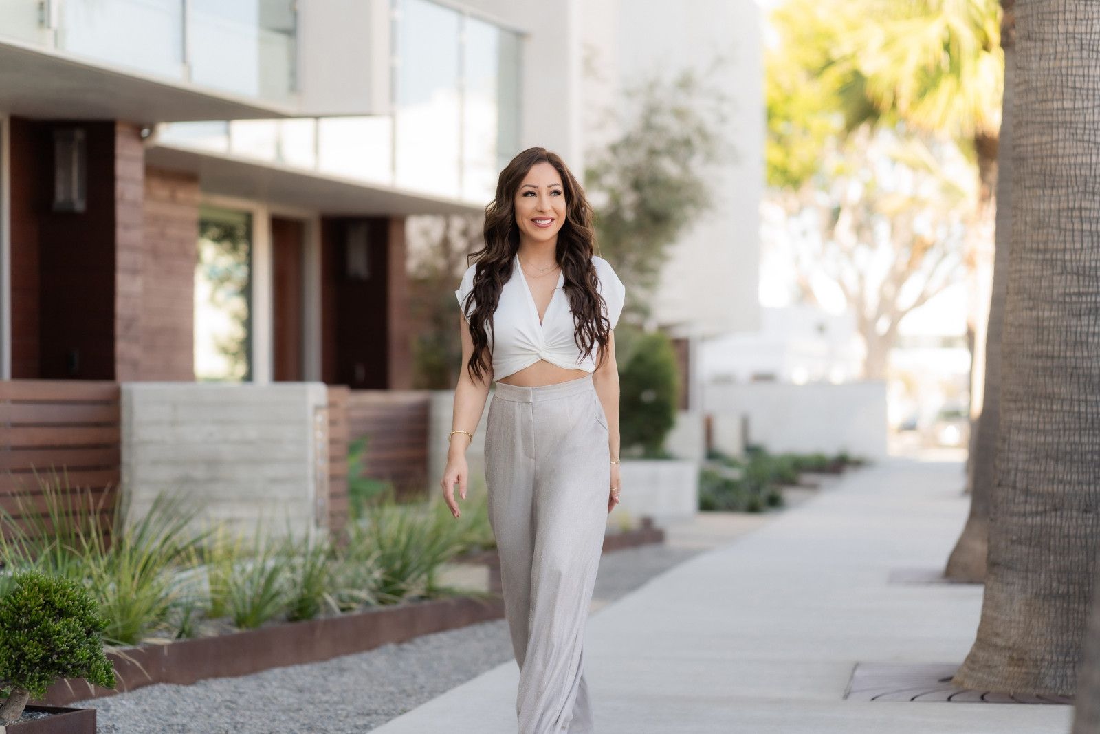 Realtor Headshots Orange County Woman walking on a sunny sidewalk beside modern apartment buildings in Newport Beach, Realtor