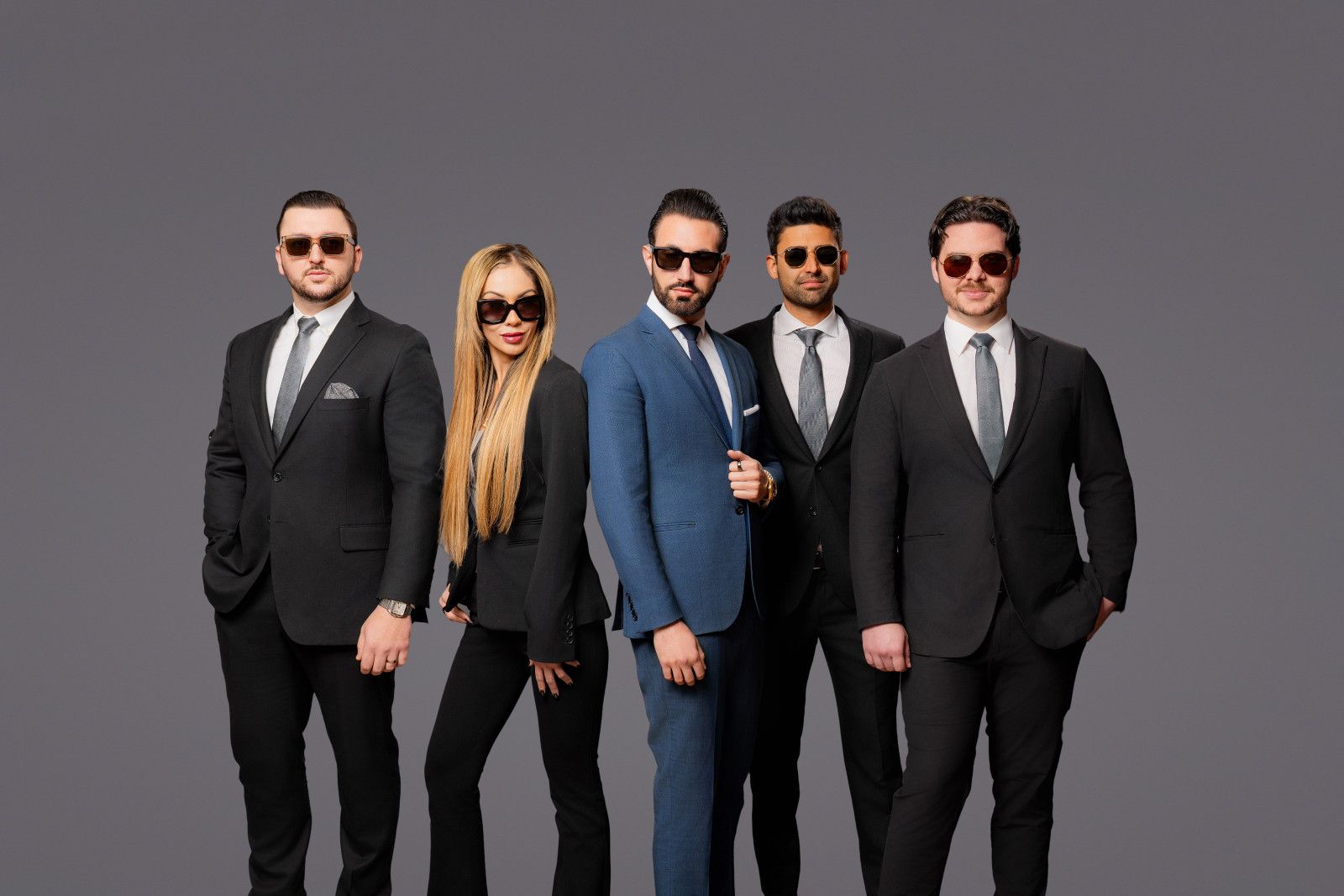 attorney brand photo in Orange County Five people in professional business suits and sunglasses standing in a line against a gray background.