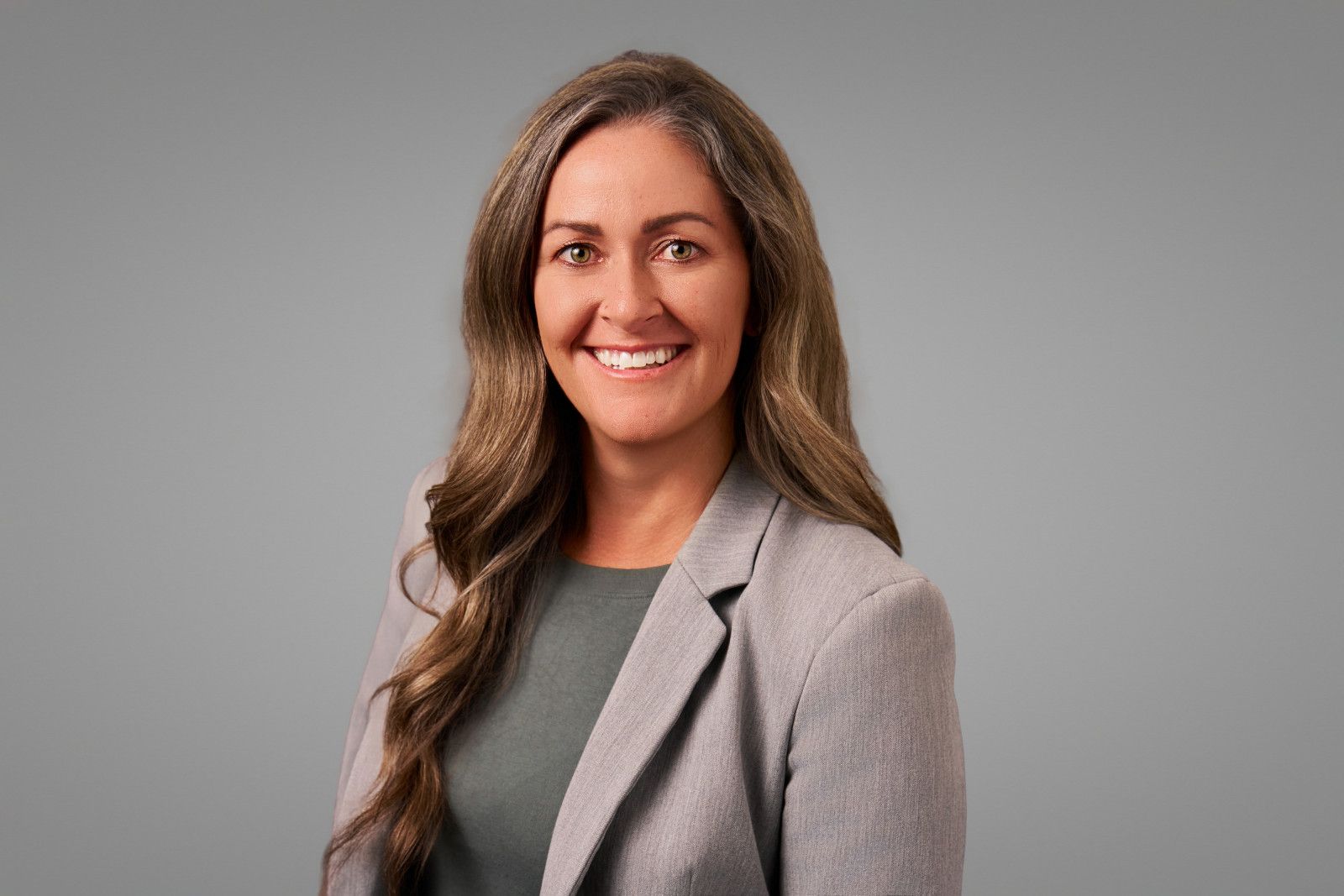 A female physician wearing gray blazer against a plain gray background being photographed during professional headshot session, Orange County CA