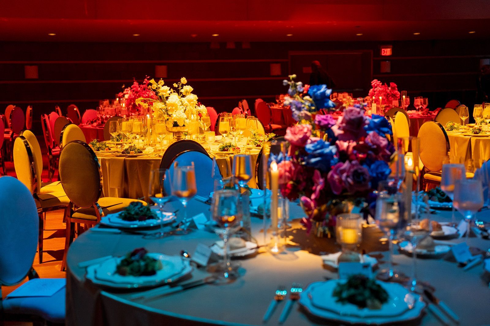 Elegant banquet tables with blue and gold floral centerpieces under warm red lighting at UCI gala