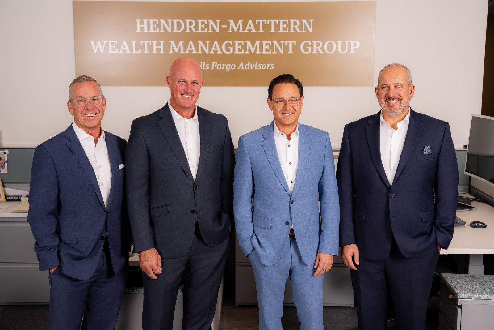 Law Firm Team headshots Orange County Four men in suits standing in a wealth management office with a company sign behind them from a Christopher Todd Studios on-site headshot session in Anaheim, California office