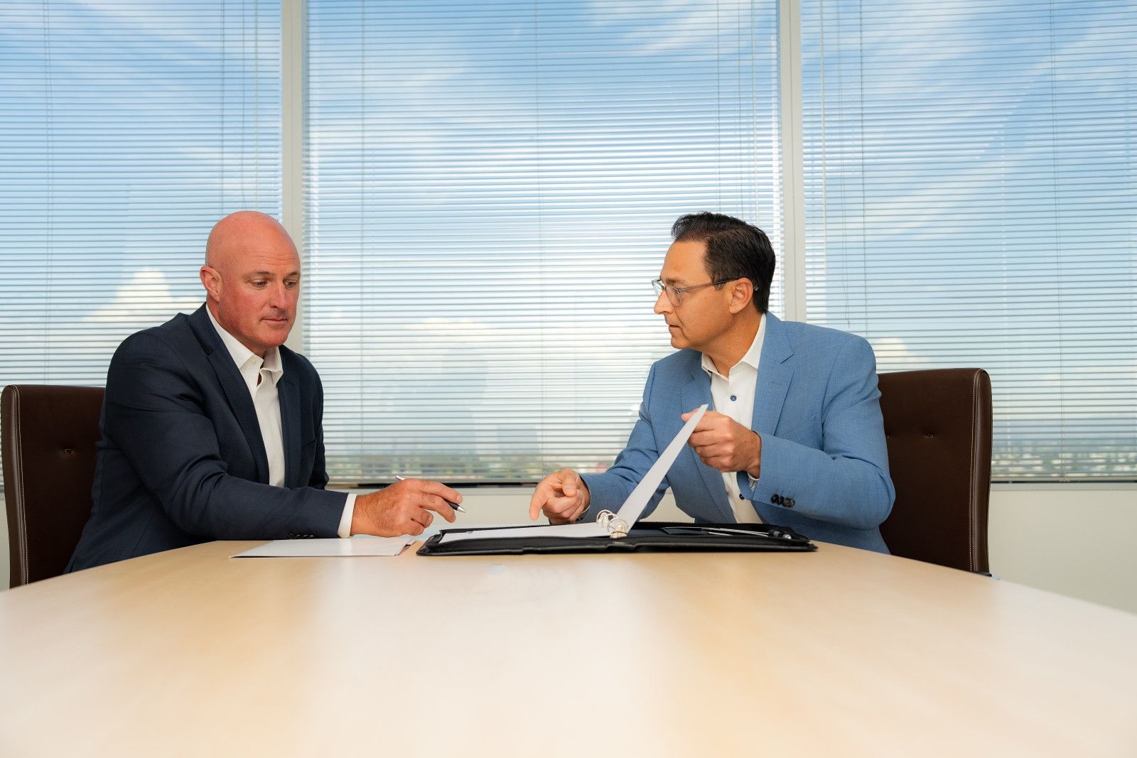 Executive Portraits headshots Two men at a table reviewing documents in a well-lit office. One points, the other writes.