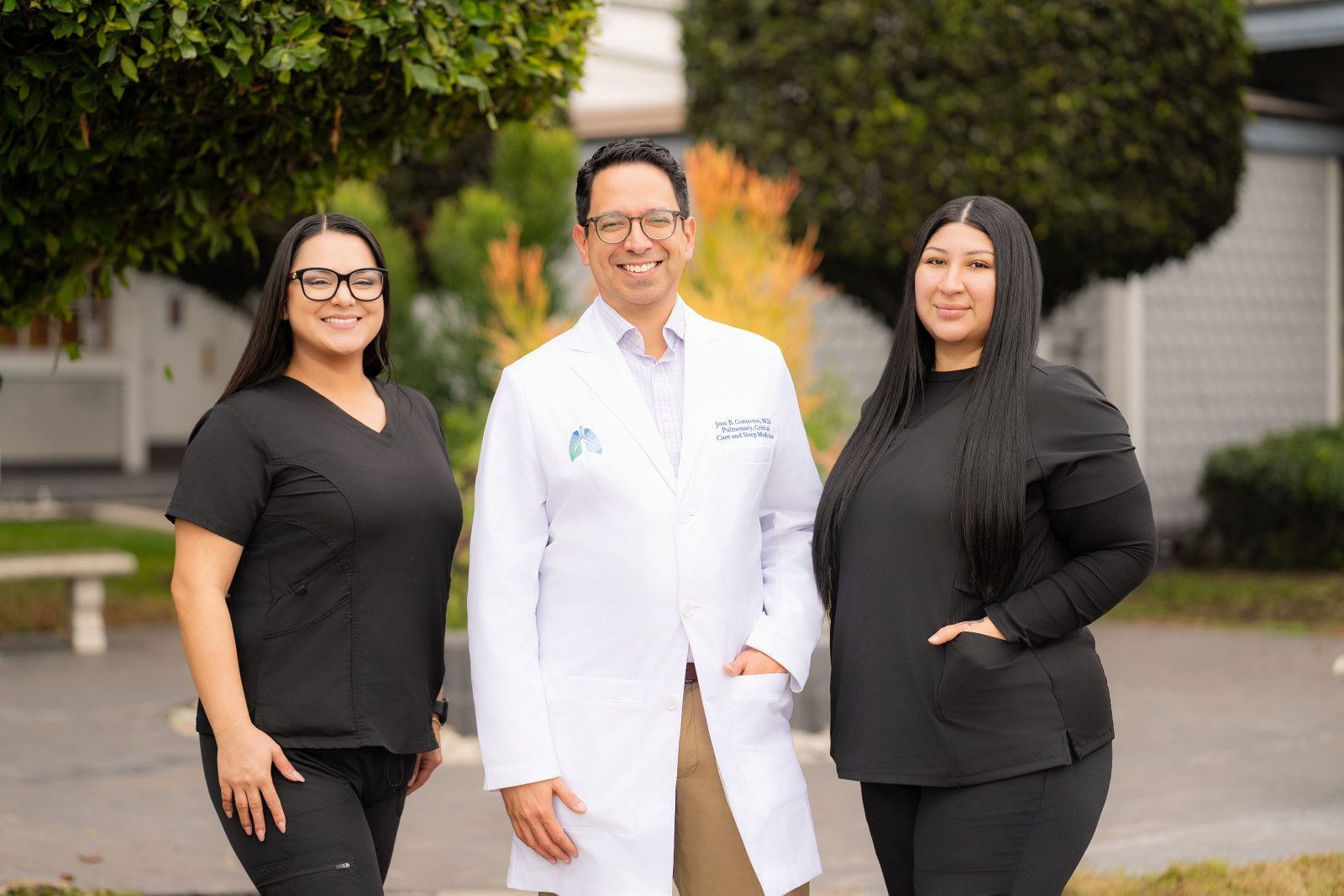 Three professionals Medical providers standing outdoors, including a doctor in a white coat, in front of a building.