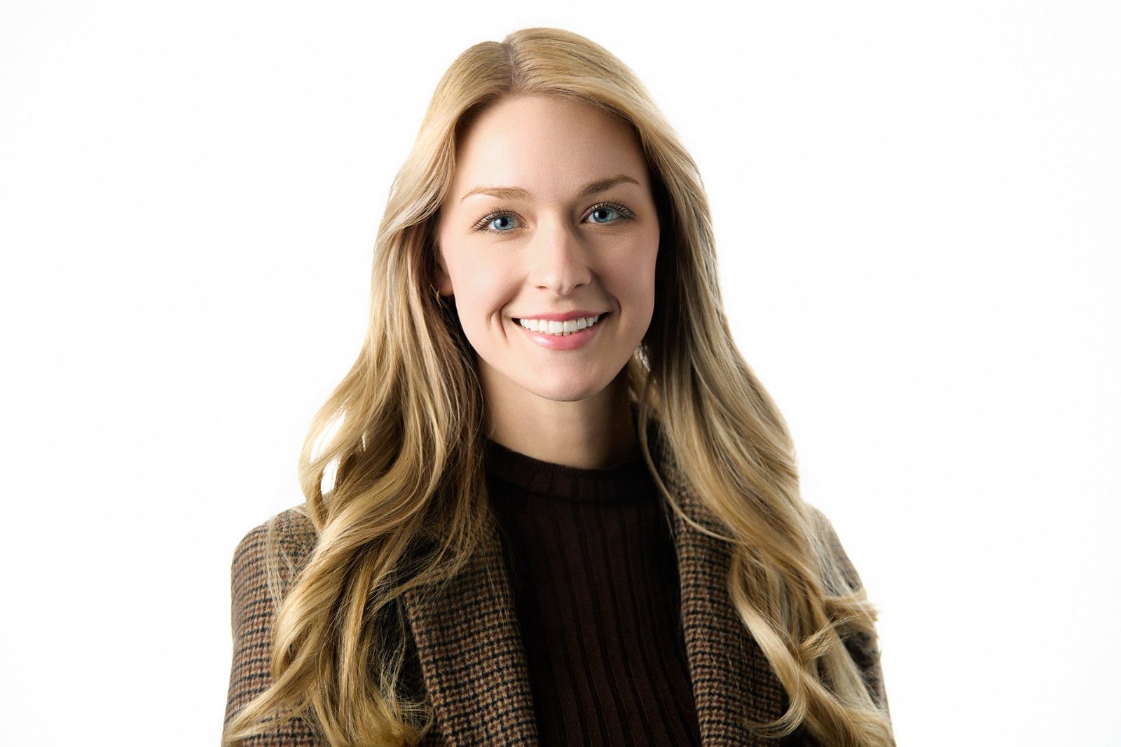 Smiling woman with long blonde hair in a dark sweater on a white background, professional brokerage headshot photo