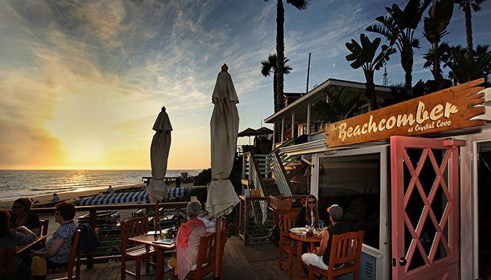 A group of people are sitting at tables outside of the beachcomber restaurant overlooking the ocean.
